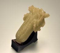 A Chinese carved pale green jadeite sculpture of a cabbage, 20th century, on a wooden stand.