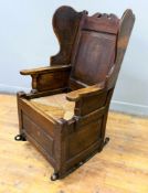 A 19thc country oak lambing chair with inset panel back, scroll top and shaped wings, with inset