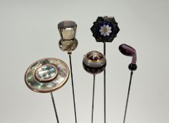 A group of five late Victorian/Edwardian hat pins: the first in amethyst glass modelled as a golf