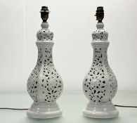 A pair of pierced white porcelain table lamps with scrolling floral foliate design, raised on