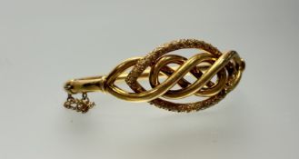 An Edwardian 9ct gold hollow stiff hinged bracelet with scrolling textured oval band and clip