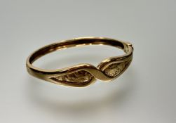 A 9ct gold cast stiff hinged bangle of cross-over design with t bar and clip locking mechanism: d. x
