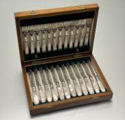 An Edwardian oak canteen containing a suite of twelve pairs of epns enraved fruit knives and forks