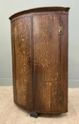 An early 20th century oak hanging corner cabinet, with inlaid geometric frieze over curved