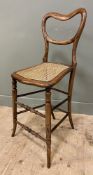 A 20th century faux rosewood beech music chair, with balloon back and caned seat, raised on turned