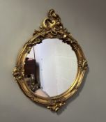 A moulded and gilded circular resin mirror with foliate and scroll detail in the Louis XVI style (l.