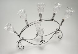 A white metal epergne, with seven etched glass flutes (a/f), raised on scrolling base. (h-36cm l-