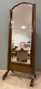 An Edwardian oak cheval mirror, with arched shaped top enclosing plate with bevelled edge, raised on