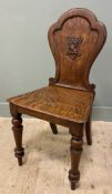 A 19th century oak hall chair, with shaped arched back decorated with carved heraldic crest, over
