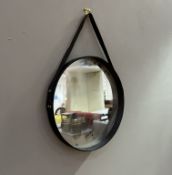 A contemporary faux leather mirror with loop handle, with the mirror plate in-set to the circular