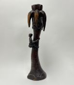An African carved wooden statue depicting a figure climbing a palm tree with rope, below palm