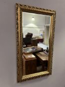 A large giltwood decorative wall mirror with carved scroll and foliate detail to border, sorrounding