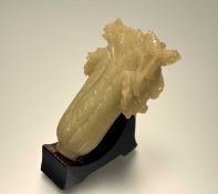 A Chinese carved pale green jadeite sculpture of a cabbage, 20th century, on a wooden stand.
