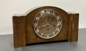 An Art Deco mantle clock in curved walnut case with stylized dial and complete with key (l. 43cm x