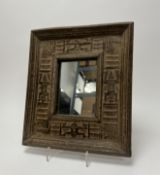A rectangular mirror set within a deeply carved wooden frame featuring geometric and stylized