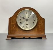 An Edwardian mahogany and inlaid mantle clock with a shaped case and raised on bracket feet, with
