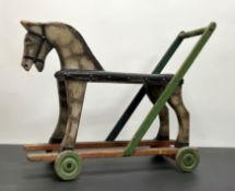 A vintage carved wooden sit-on model of a horse push-along toy, on four wheels with leather seat and