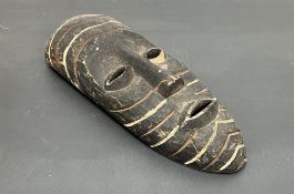 A tribal wooden mask of elongated form with carved detail, possibly Papua New Guinea (l. 39cm)