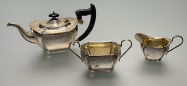 A Sheffield silver three piece scalloped panel sided tea service with ebinized wood handle and knop: