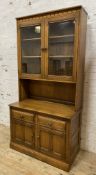 A modern two-part kitchen dresser by Ercol, with carved cornice over twin glazed panel doors to top,