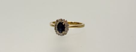 A 18ct gold cluster ring set oval facet cut sapphire approximately 0.5ct within a surround of ten