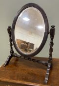 An Edwardian oak swing mirror, bevelled oval plate raised on barley twist supports and splayed feet: