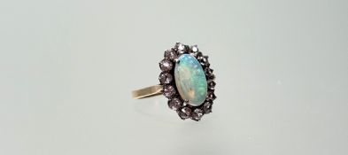 A yellow metal ring set with an oval fire opal within a surround of fourteen moissanite round