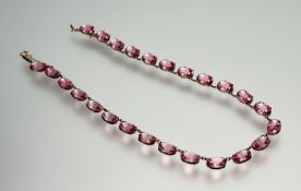 An Edwardian 9ct riviere necklace set twenty five oval pink topaz with a barrel clasp fastening