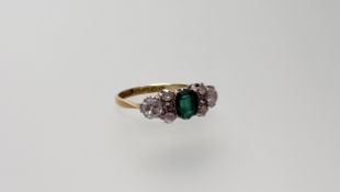 An Edwardian 18ct gold ring set oval cut emerald flanked by three old mine cut diamonds and single
