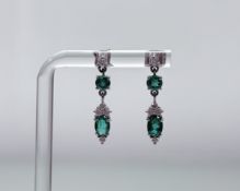 A pair of 9ct white gold drop earrings each set with an oval, enhanced emerald approximately 0.3ct