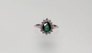 An emerald and diamond cluster ring, the pear-cut emerald within a band of fourteen round
