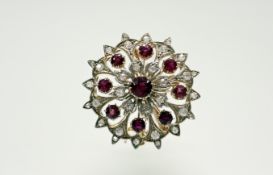 An Eastern yellow and white metal circular pendant brooch set with red coloured stones within a