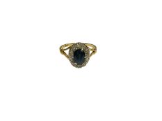Sapphire and diamond cluster ring with an oval mixed cut blue sapphire surrounded by a border of sin