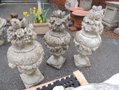 FOUR RECONSTITUTED STONE GARDEN URNS, festooned with fruits, 80cms (h) Provenance: The Cornelia