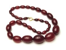 STRING OF CHERRY COLOURED AMBER STYLE GRADUATED BEADS, the largest 27mm, with gold coloured bolt