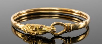 18CT GOLD EQUESTRIAN BANGLE, London import marks, 1985 (one ruby eye missing), cuff size 55mms, 15.