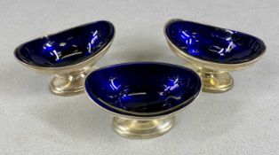 GEORGE III SET OF THREE SILVER OVAL PEDESTAL SALTS, all with blue glass liners, Robert Hemmell I,