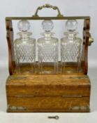 EDWARDIAN BETJEMANN'S PATENT TANTALUS, oak with metal mounts, containing three square cut-glass