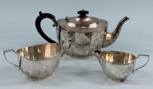 GEORGE V SILVER THREE-PIECE TEA SERVICE of oval panelled form, teapot with ebonised handle and