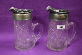 A pair of early 20th century white metal mounted jugs, each with generous spout, applied loop
