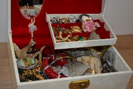 A cream musical jewellery box, containing an assortment of costume jewellery, including brooches,