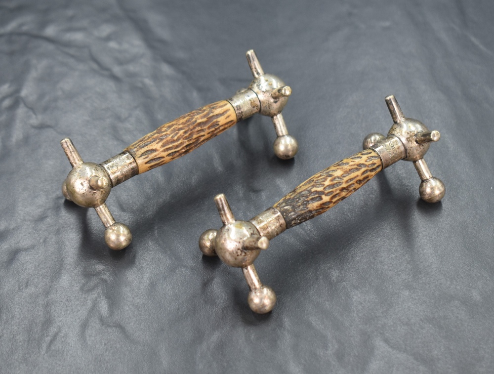 A pair of white metal and antler knife rests, of traditional form having central antler bars, raised