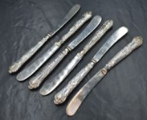 A set of six late Edwardian silver handled butter knives, having decorative embossed scroll work
