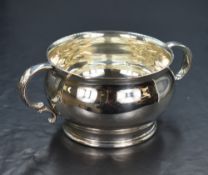 A George V silver sugar bowl, of circular form having a flared rim and two scroll handles, on a