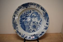 A large 19th century Delft plate, hand coloured with blue and white foliage within a garden setting,