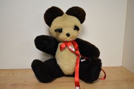 An early 20th century panda teddy bear, having a red bow-tie, glass eyes, swivel legs and arms,