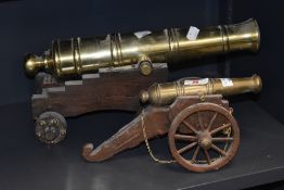 A pair of miniature solid brass table top cannons, mounted on a wooden wheeled base, largest