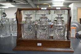 A quality mid-20th century oak Tantalus with brass handle, the three crystal cut decanters having