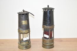 Two early 20th century brass miners safety lamps, one having a red glass eye, the other numbered '
