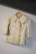 An early twentieth century childrens fur coat, in white-beige, probably rabbit. Has some staining to